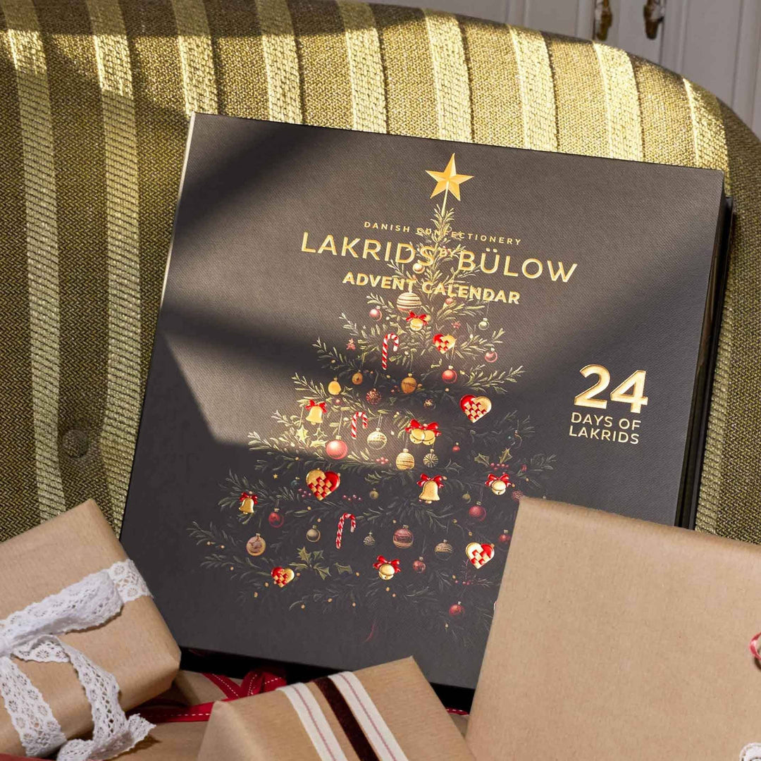 Chokladshopen Lakrids By Bülow adventskalender med svart och guldig julgransillustration och 24 luckor för gourmetlakrits