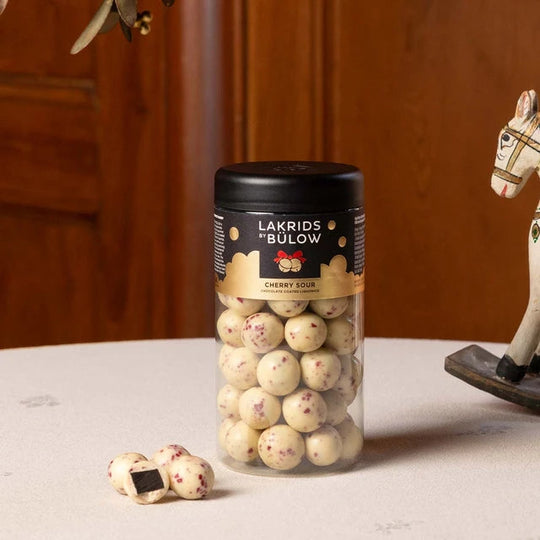 Chokladshopen Lakrids By Bülow Cherry Sour lakritskulor med vit choklad och körsbärsgranulat i en svart burk.