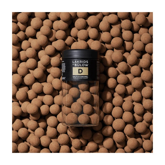 Chokladshopen Lakrids By Bülow D salt och karamell lakritskulor i en genomskinlig burk omgiven av lakritskulor.