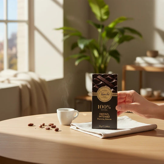 Chokladshopen Venchi 100% mörk chokladkaka i elegant förpackning bredvid en kopp espresso och kakaobönor på ett bord.