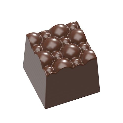 Glansig mörkbrun chokladpralin med distinkt bubbeltextur och vinklade sidor